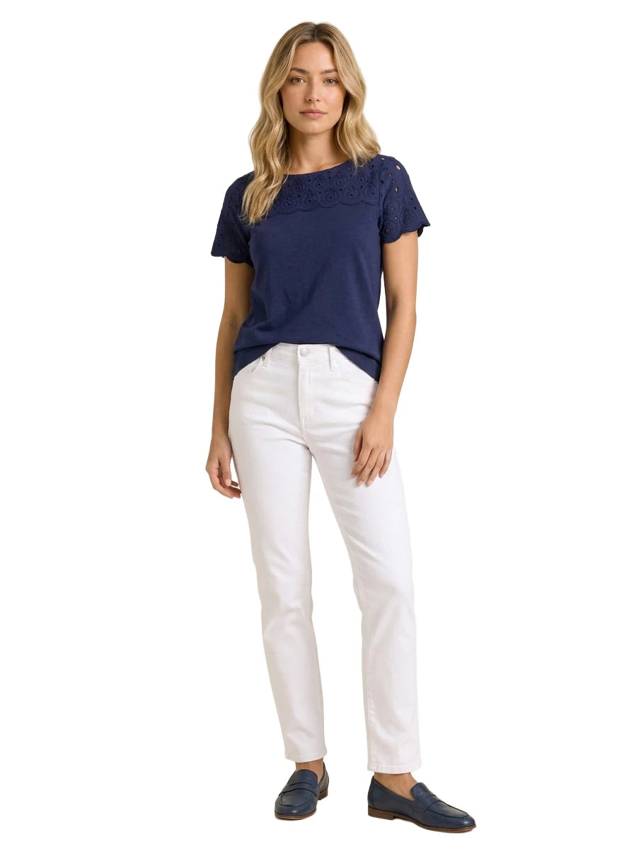 Full-length front view of a woman modeling a Charter Club navy blue eyelet-trim top paired with white slim-fit jeans and navy leather loafers.