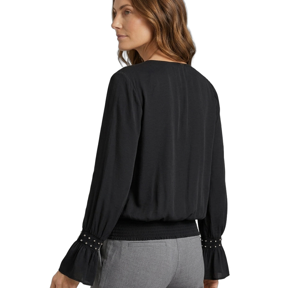 Woman wearing a black blouse with long sleeves and gray pants on a white background