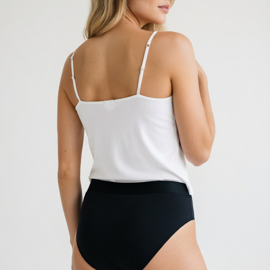 A woman shown from the back wearing a white camisole-style top with thin straps and black high-waisted bottoms against a plain light gray studio background.