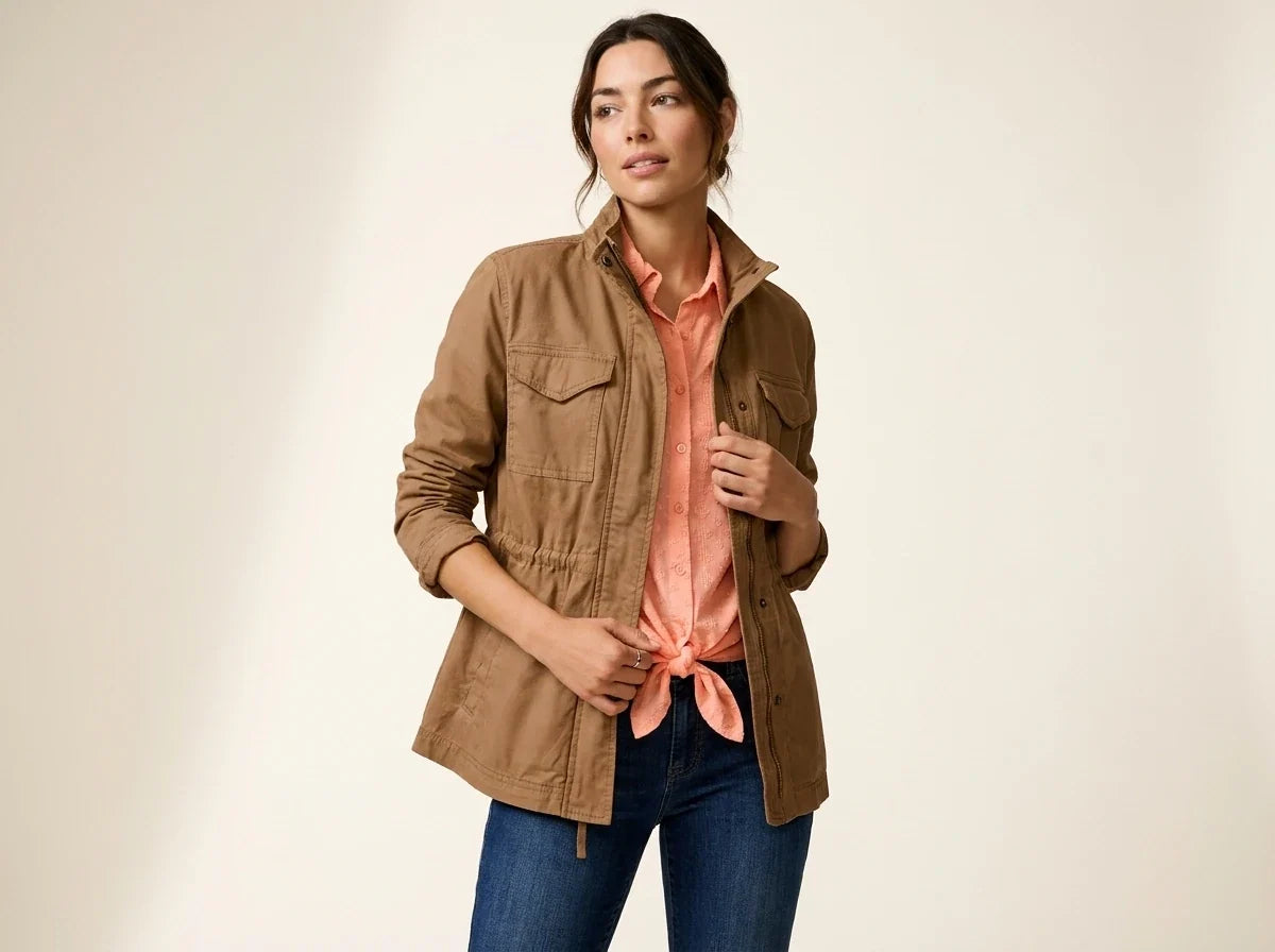 Brunette woman modeling a camel brown utility jacket with flap pockets over a peach tie-front button-down shirt and blue jeans.