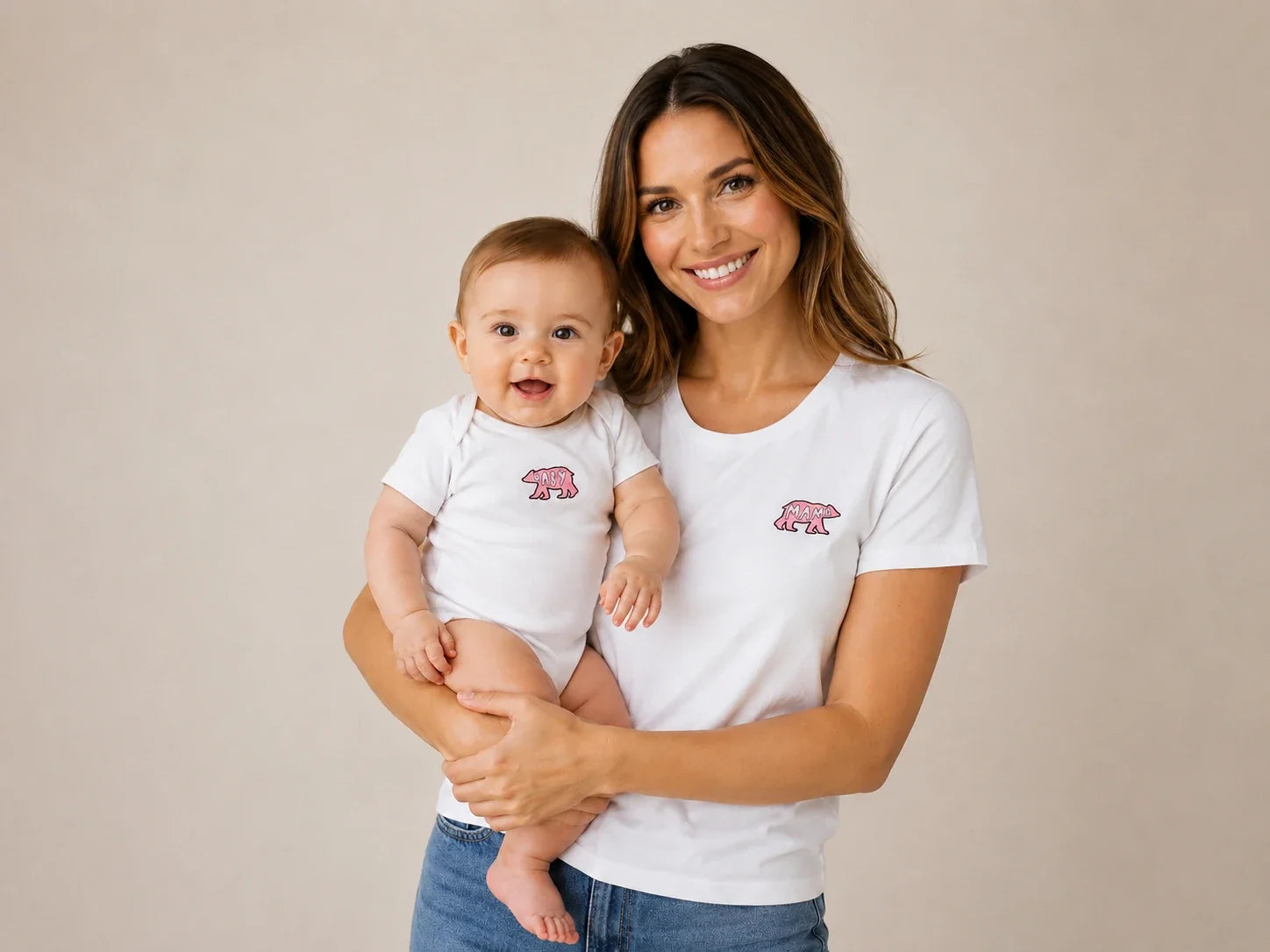 Mother holding her smiling baby wearing matching white shirts with pink 'Mama Bear' and 'Baby Bear' graphics.