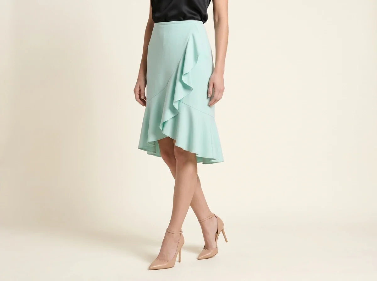 Cropped view of a woman wearing a light mint green ruffled midi skirt, black top, and nude pointed-toe ankle-strap pumps against a neutral studio backdrop.
