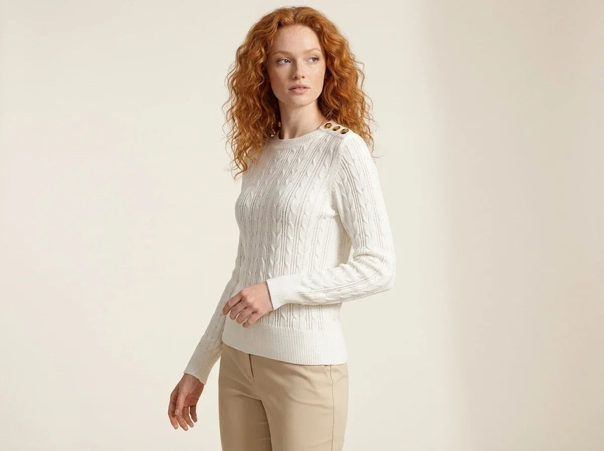 Woman with curly red hair modeling an ivory cable-knit crewneck sweater with shoulder button details, paired with khaki trousers[cite: 29].