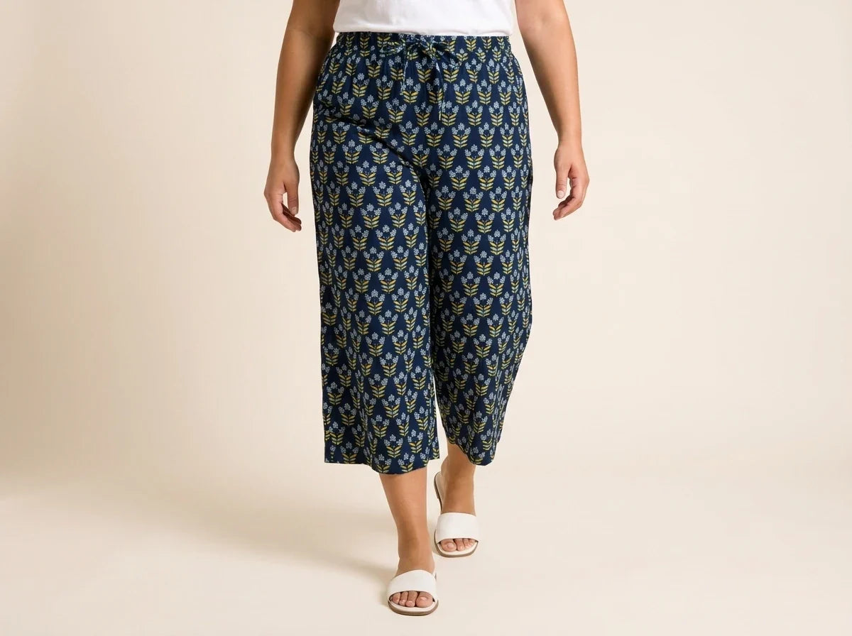 Cropped view of a woman wearing navy blue floral print wide-leg culotte pants with a drawstring waist and white slide sandals.