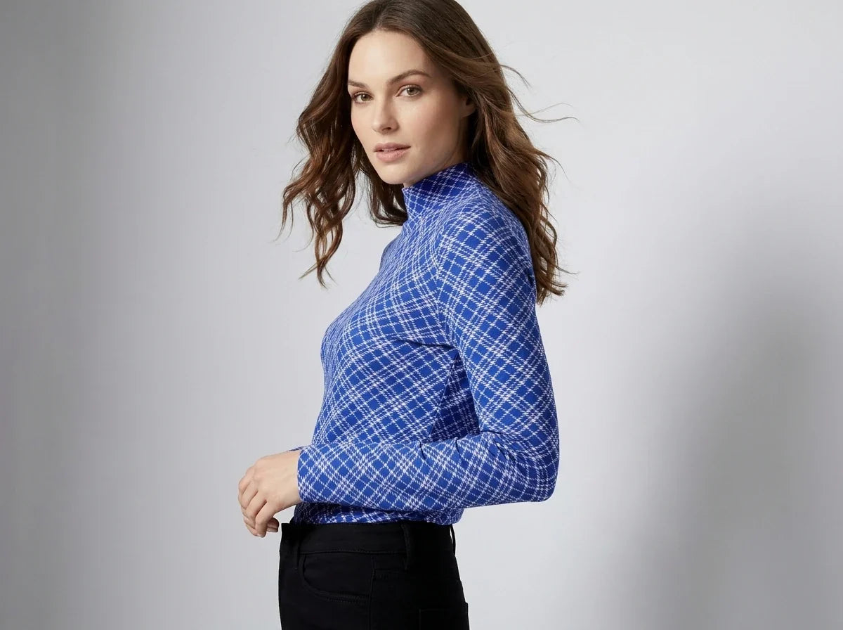 A woman wearing a blue and white plaid mock neck long-sleeve shirt, paired with black pants, photographed against a neutral gray studio background.