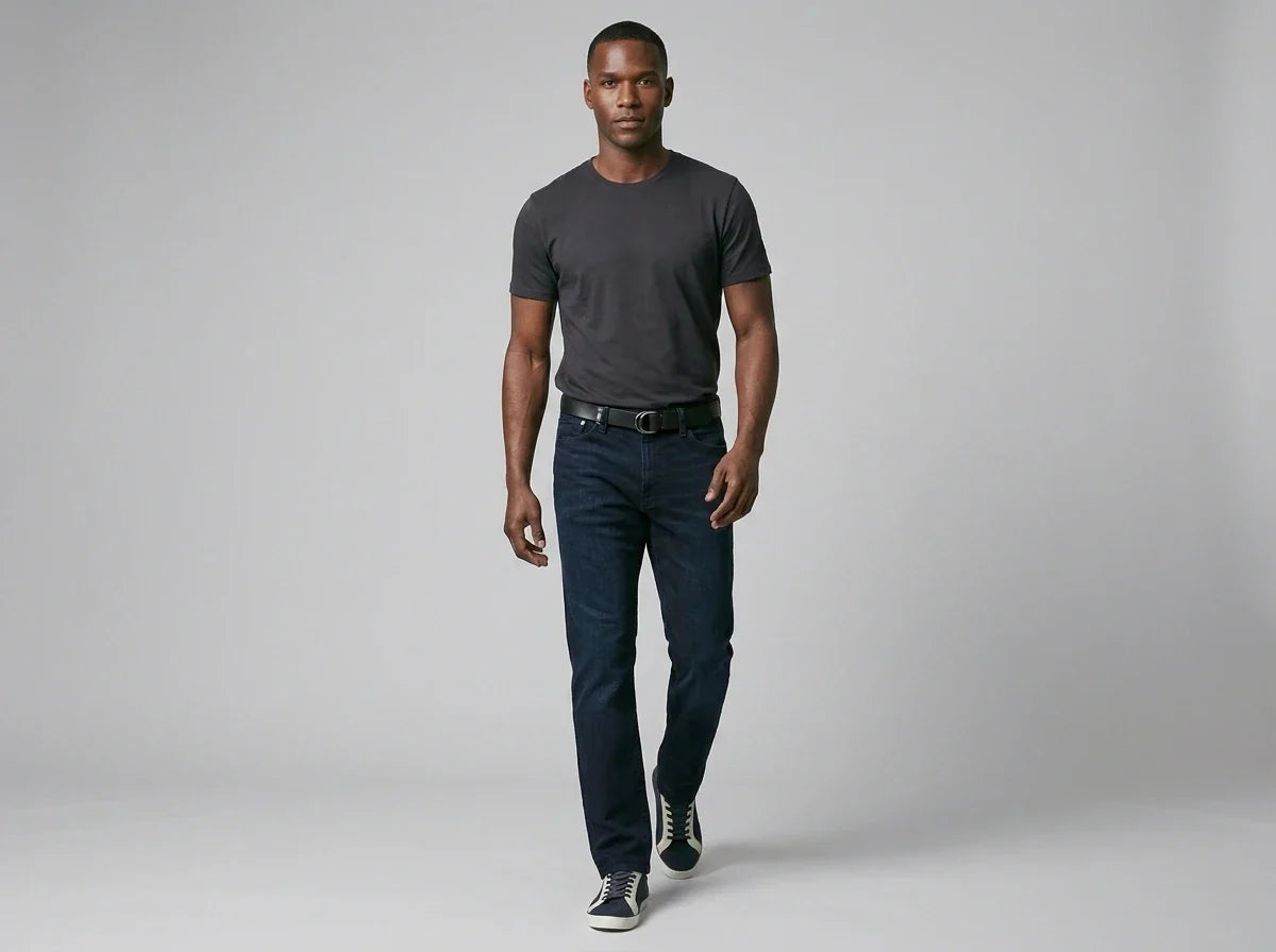Recommended Alt Text (Concise & SEO-Friendly):
"Man walking forward wearing a dark charcoal crewneck t-shirt, dark wash straight-leg jeans, a black belt, and casual low-top sneakers