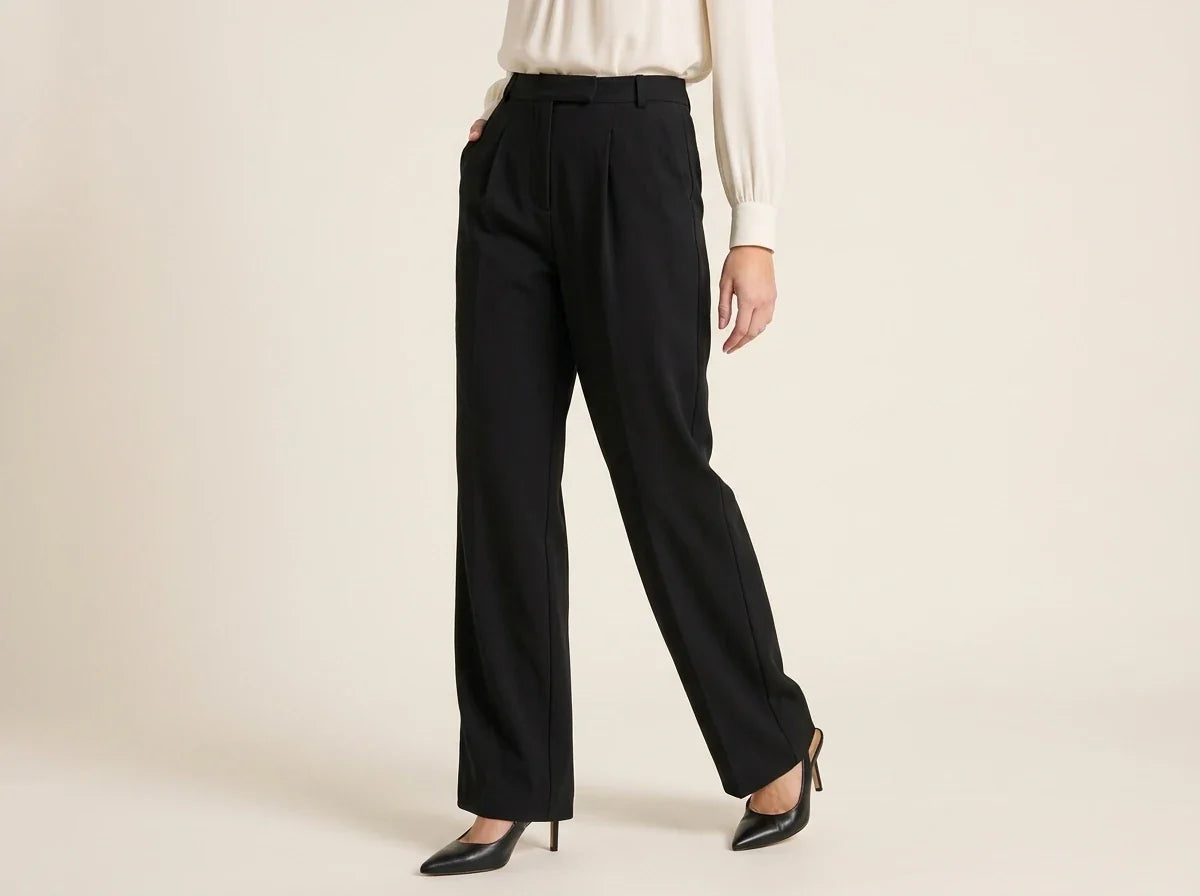 Cropped view of a woman wearing high-waisted pleated black wide-leg trousers paired with pointed-toe slingback heels and a cream blouse.