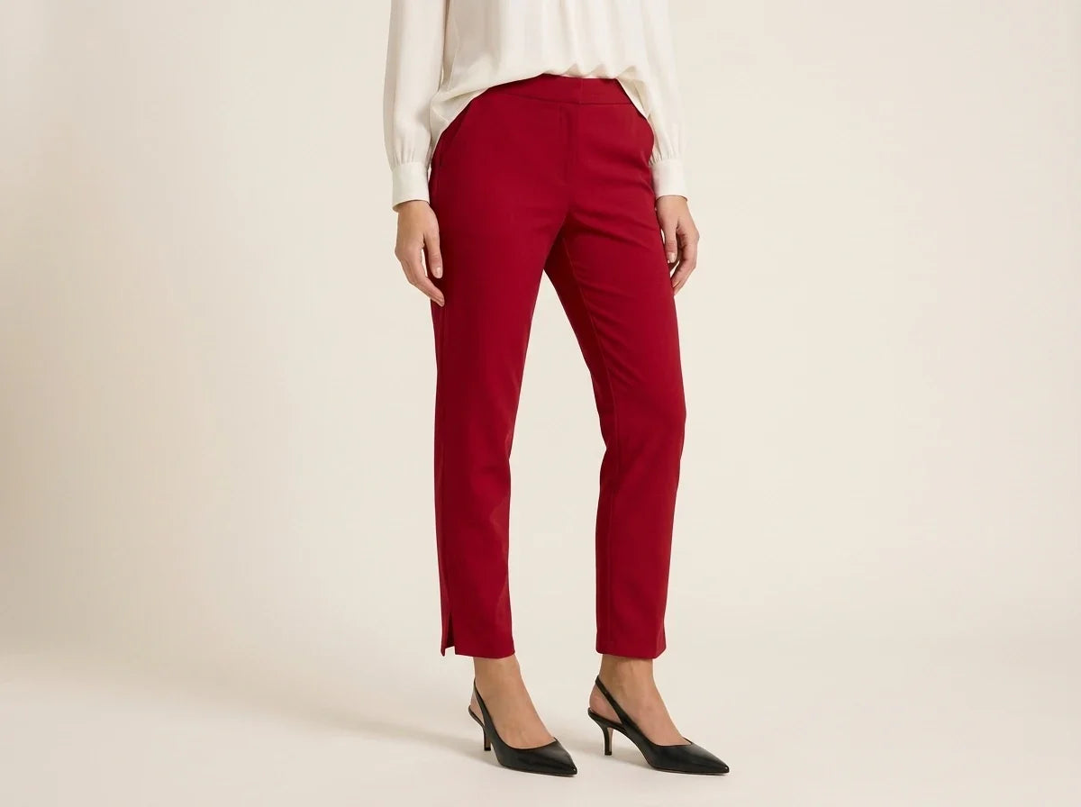 Cropped view of a woman wearing red slim-fit pull-on ankle trousers with side hem slits, styled with black slingback heels and a cream blouse.