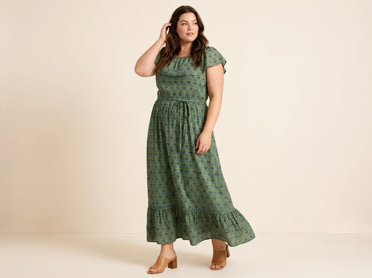 Brunette woman modeling a plus-size olive green floral maxi dress with flutter sleeves, a tie waist, and tan block heel sandals.