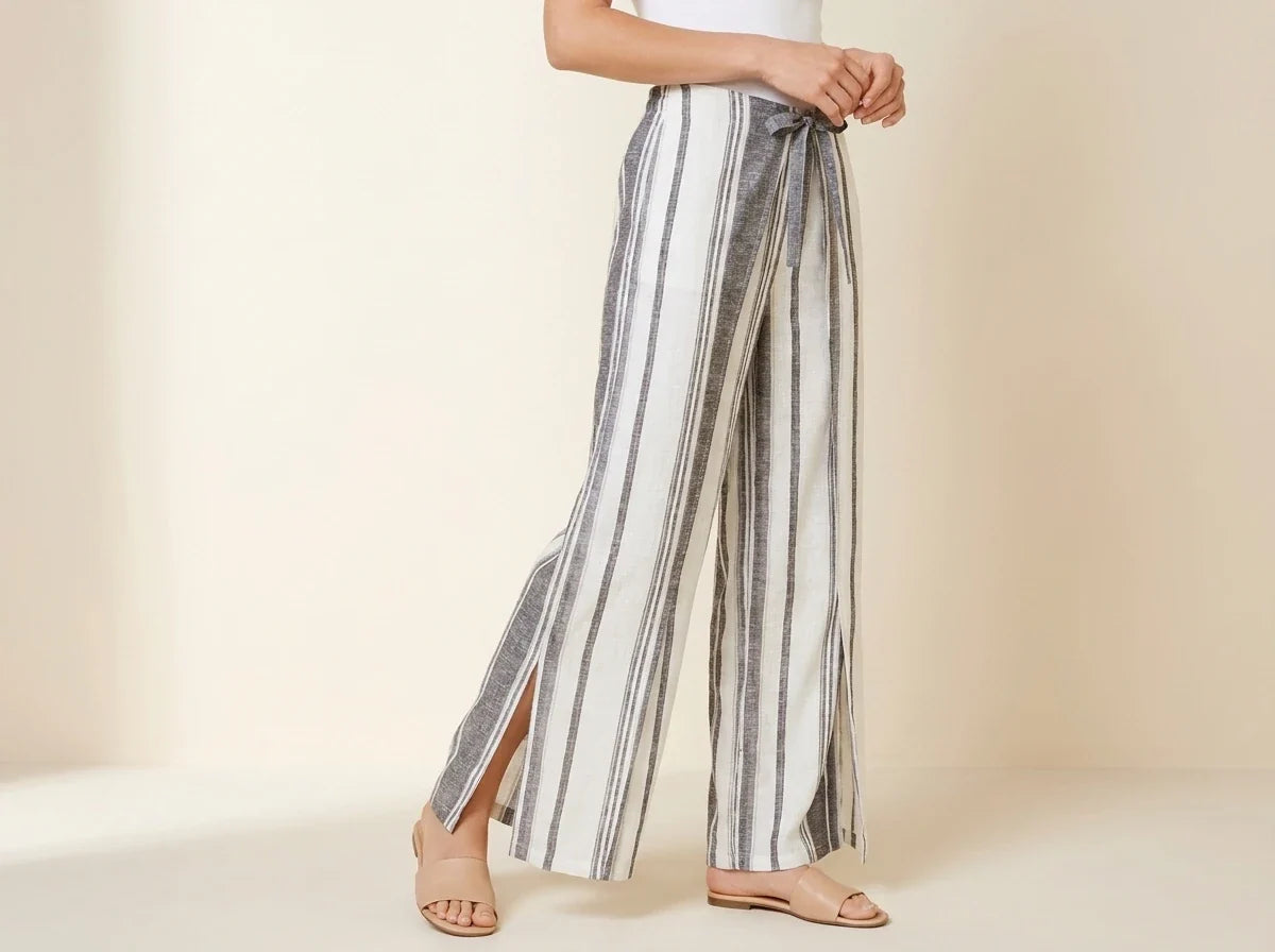 Cropped view of a woman wearing black and cream striped wide-leg linen pants with high side slits and nude leather slide sandals.