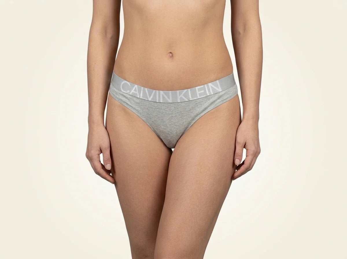 Cropped view of a woman wearing heather grey Calvin Klein cotton thong underwear with a signature logo elastic waistband[cite: 35].