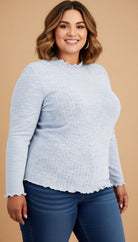 Woman wearing a light blue textured top and dark blue jeans on a beige background