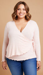 Woman wearing a light pink long-sleeve top and blue jeans on a beige background
