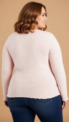 Woman wearing a light pink sweater and blue jeans on a beige background