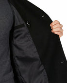 Close-up of a person wearing a black coat with a gray sweater underneath, on a white background.