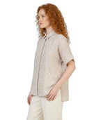 Woman wearing a beige patterned shirt and white pants on a white background