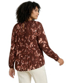 Woman wearing a brown patterned blouse with white pants on a white background