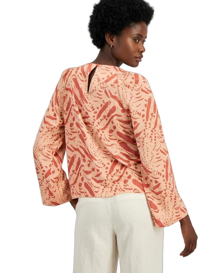 Woman wearing a patterned peach blouse and white pants on a white background