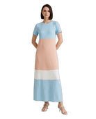 A woman modeling a short-sleeve maxi dress with a colorblock design in light blue, peach, white, and light blue, paired with white heeled sandals against a plain white background.