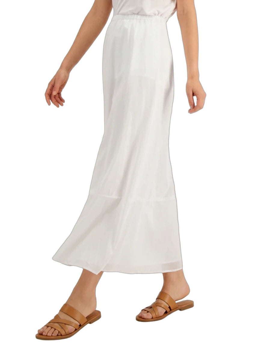 A model wearing a white tiered maxi skirt with a smocked waistband, paired with tan slide sandals, shown against a plain white background.