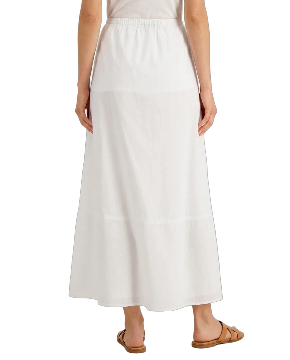 A woman wearing a long white tiered maxi skirt with an elastic waistband, paired with brown flat sandals, shown from the back against a plain white background.