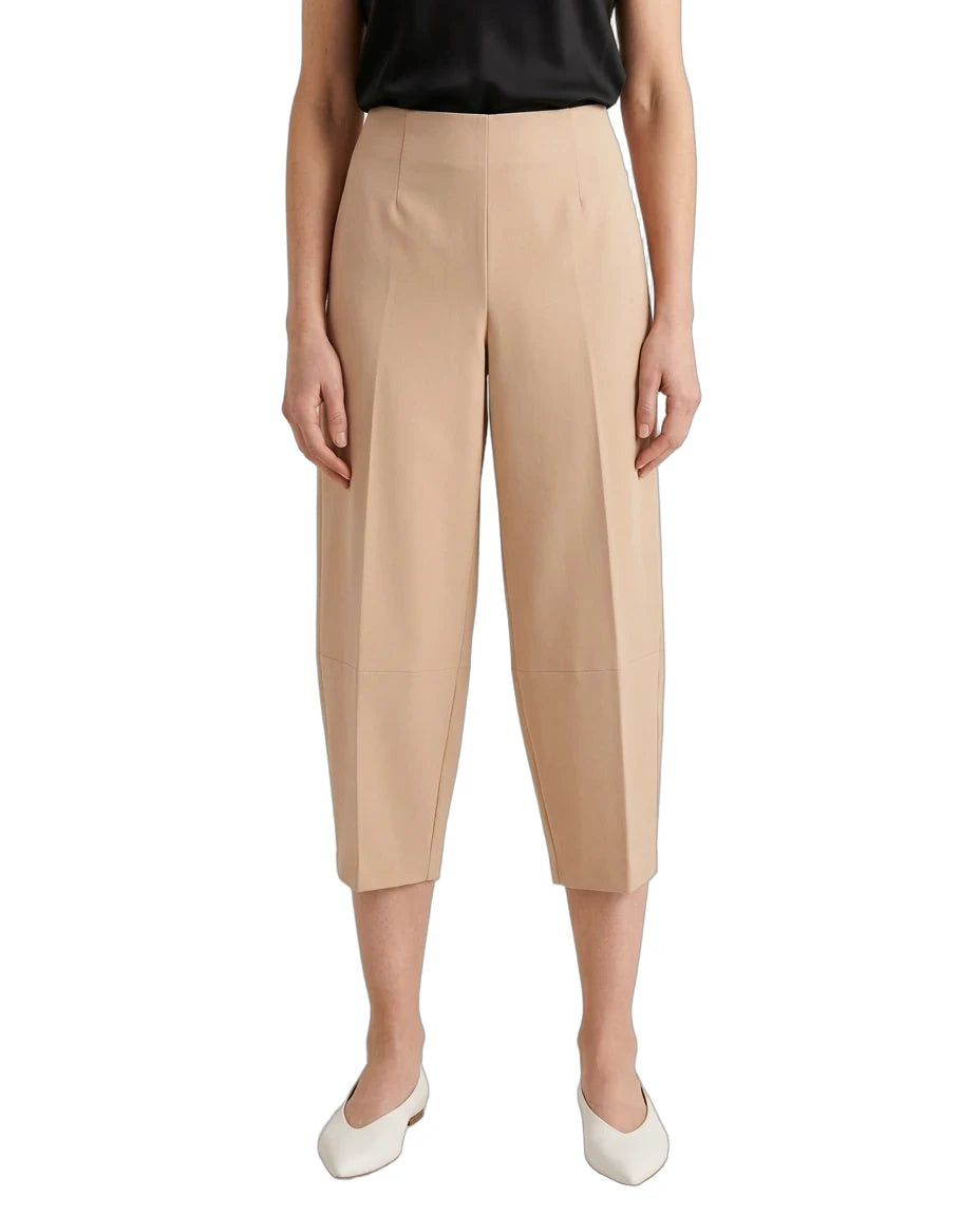 A model wearing beige cropped capri pants with a subtle sheen, paired with a black top and white pointed flats, shown against a plain white background.