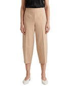 A model wearing beige cropped capri pants with a subtle sheen, paired with a black top and white pointed flats, shown against a plain white background.
