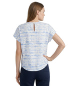 A woman shown from the back wearing a short-sleeve top with a light blue and white abstract pattern and a small keyhole cutout at the back neckline, paired with dark navy pants, against a plain white background.