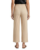 A person shown from the back wearing high-waisted, wide-leg cropped pants in a light beige or sand color, paired with a black top and flat sandals, against a plain white studio background.