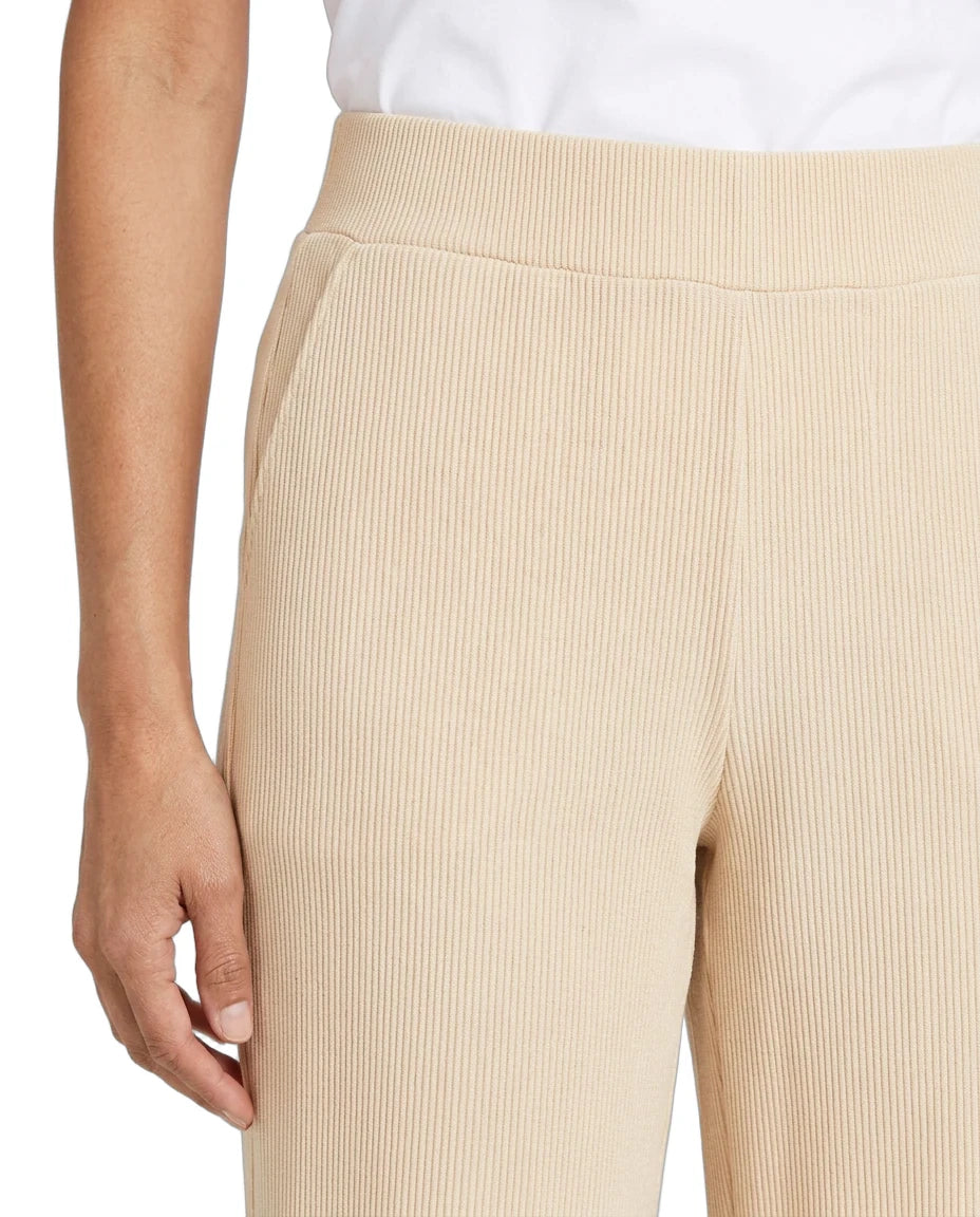 Close-up of a person wearing ribbed knit pants in a light beige or cream shade, paired with a white top. The photo focuses on the texture and fit of the pants, with a plain white background.