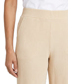 Close-up of a person wearing ribbed knit pants in a light beige or cream shade, paired with a white top. The photo focuses on the texture and fit of the pants, with a plain white background.