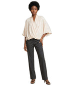 A model wearing a cream-colored, draped short-sleeve top and dark charcoal gray straight-leg trousers, paired with brown strappy heels, against a plain white background.