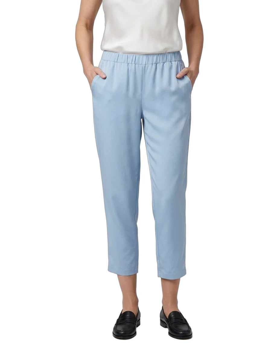 A model wearing light blue cropped trousers with an elastic waistband and side pockets, paired with a white top and black loafers, shown against a plain white background.