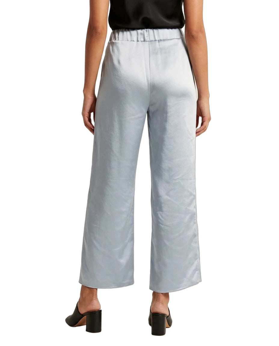 A model from the back wearing light blue wide-leg cropped trousers with a satin-like sheen, paired with a black top and black block-heel mules, against a plain white background.