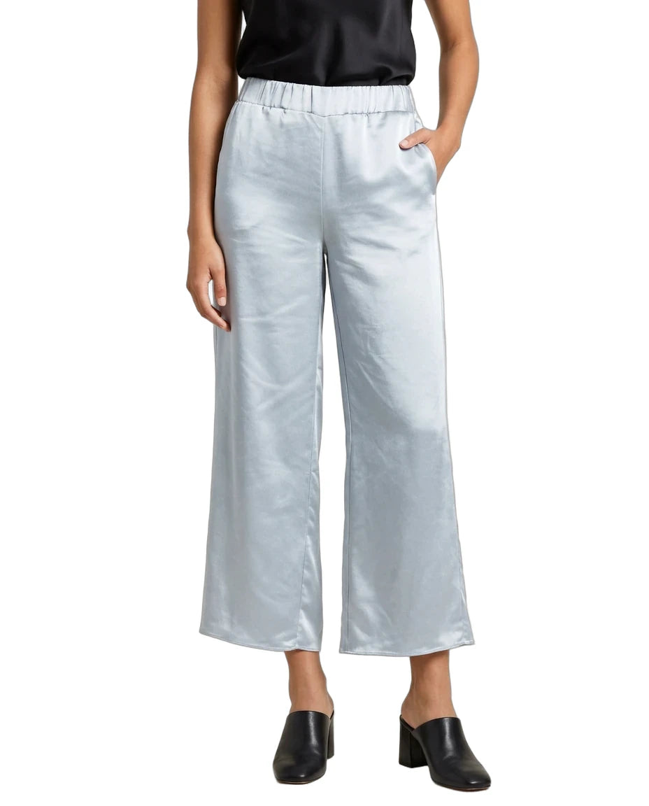 A model wearing light silver wide-leg cropped pants with an elastic waistband, styled with a black satin top and black leather mule shoes against a plain white background.