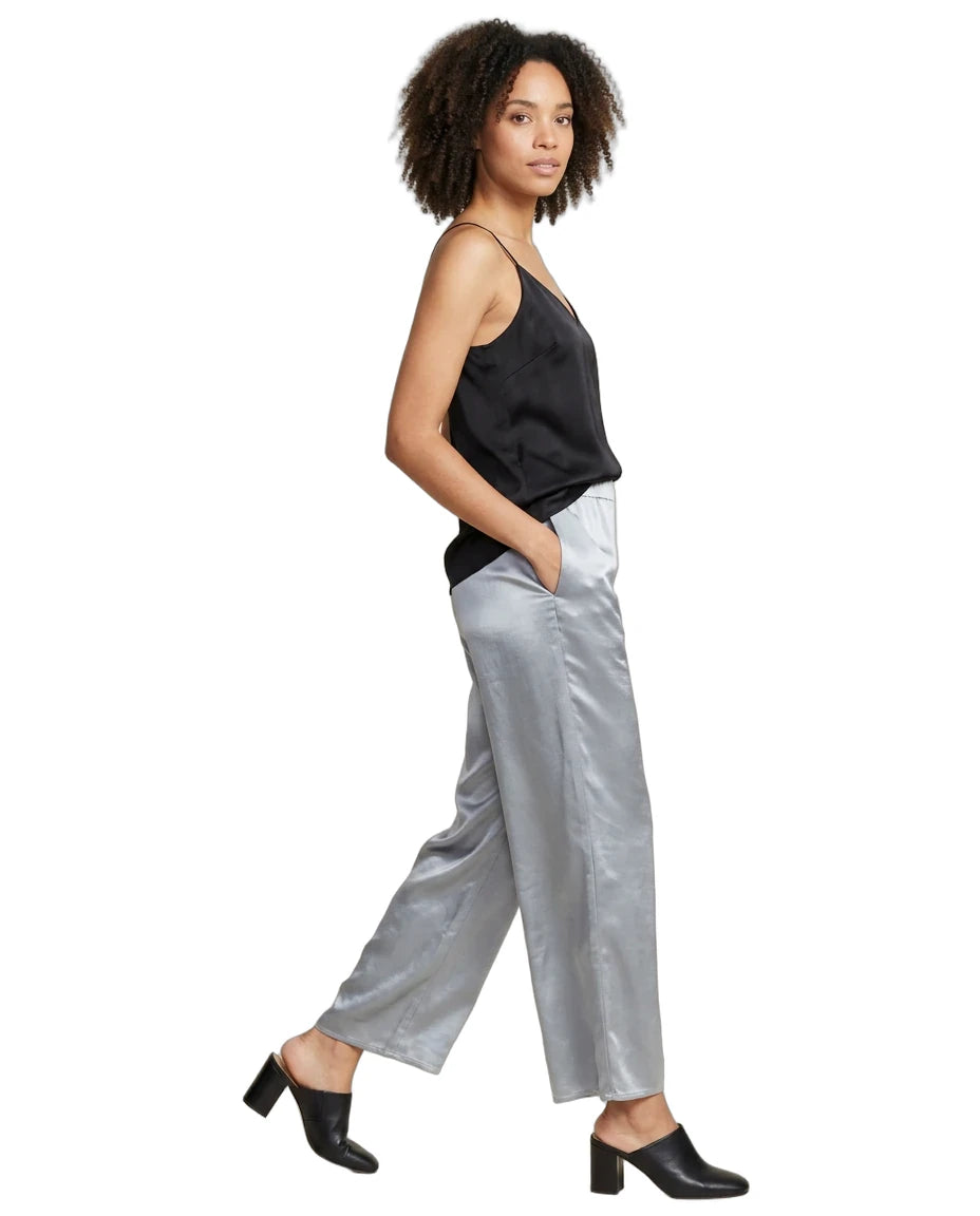 A woman modeling a black satin camisole and shiny silver satin wide-leg trousers, paired with black mule heels, against a plain white background.