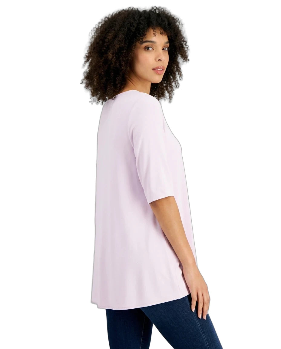 A woman with curly dark hair is shown from the side/back wearing a light pink short-sleeve tunic top and dark blue jeans against a plain white background.