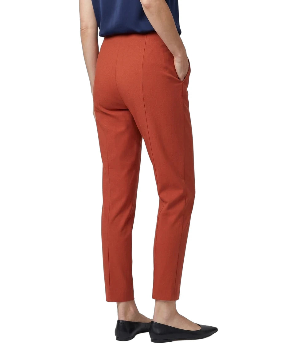 A person shown from the back wearing rust-orange cropped trousers, a navy top, and black flats against a plain white studio background.