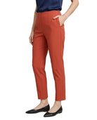A model wearing a pair of cropped, straight-leg trousers in a warm rust orange color, paired with a navy top and black flats, shown from the waist down on a white background.