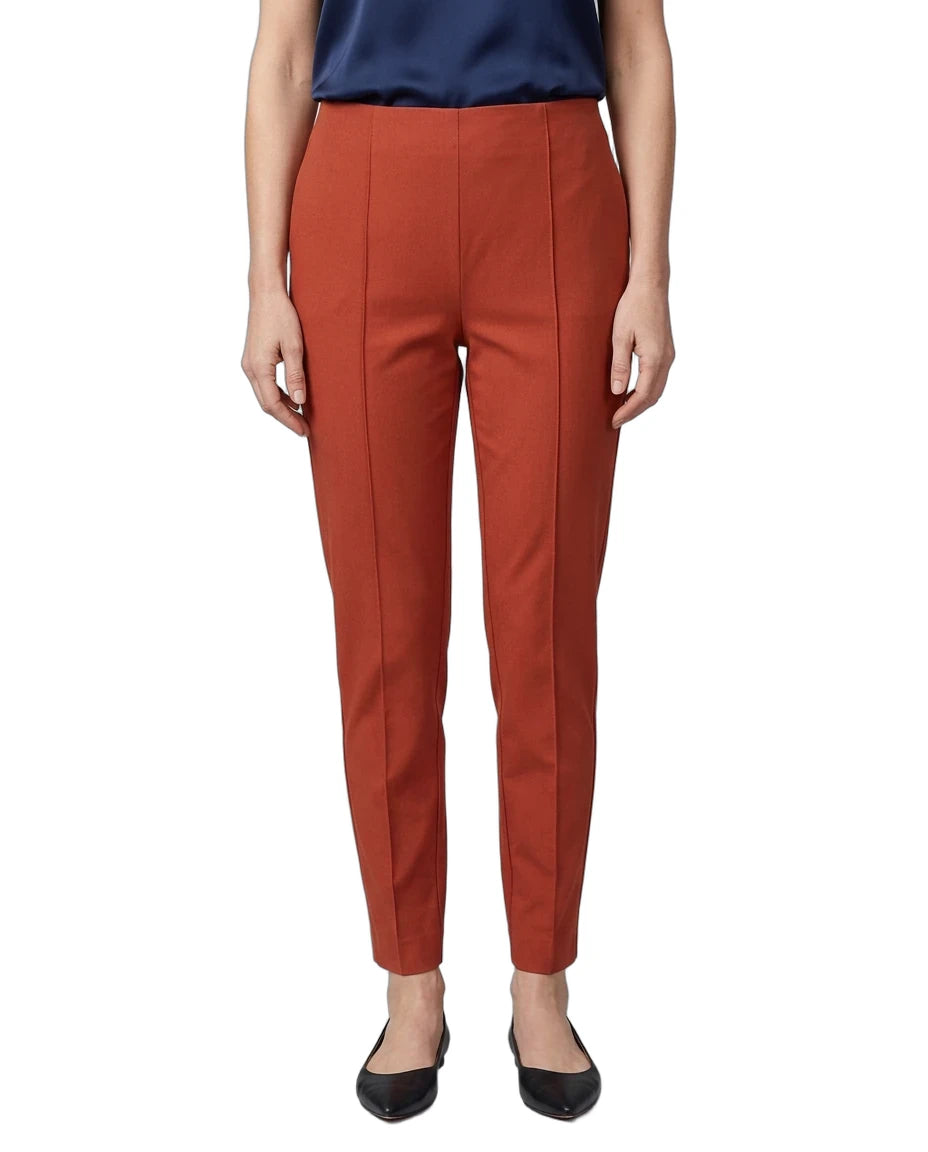 A model wearing a pair of rust-orange cropped trousers with front crease details, paired with a navy top and black flats, shown against a plain white background.