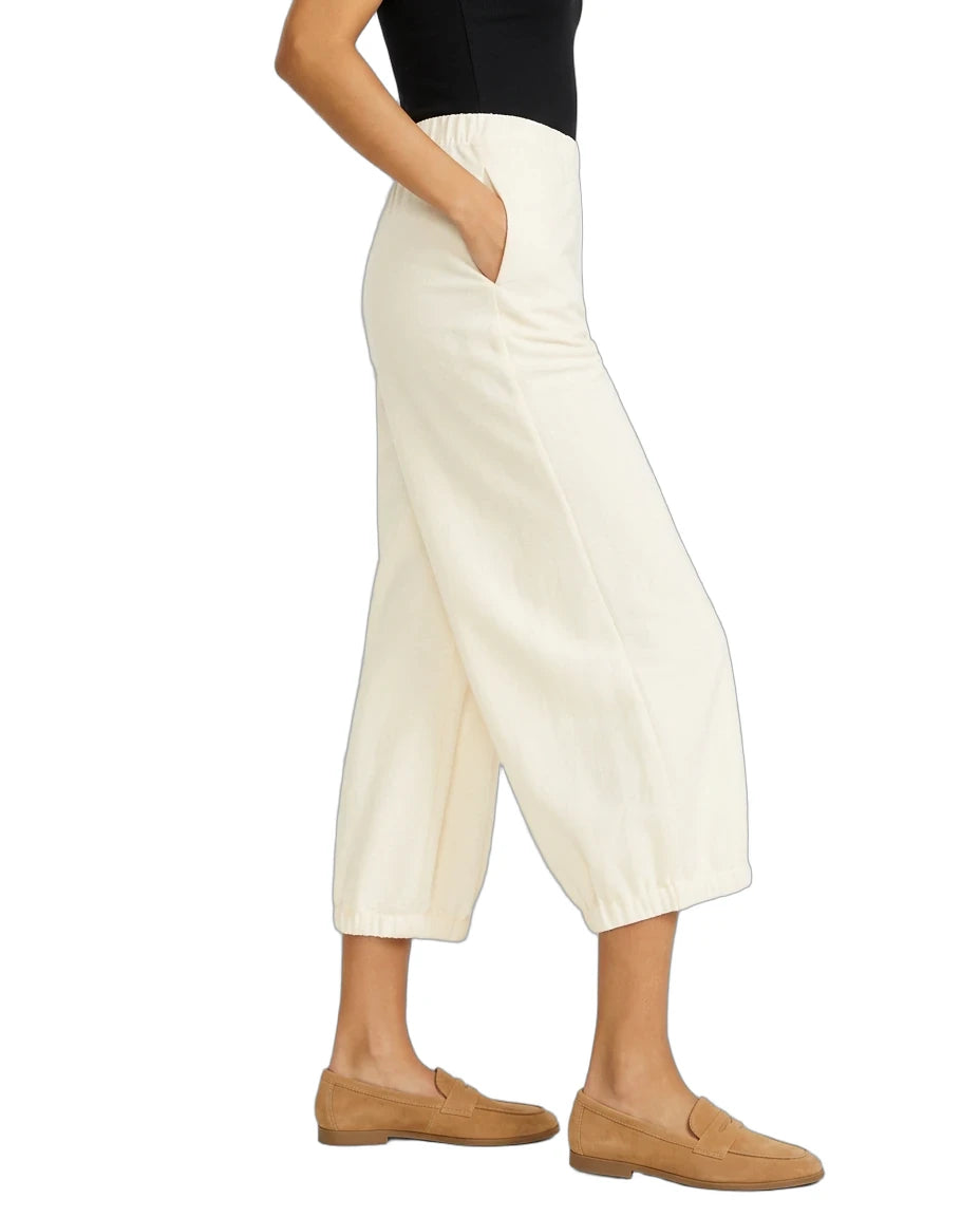 A person wearing off-white cropped wide-leg pants with side pockets, paired with a black top and tan loafers, shown against a plain white background.