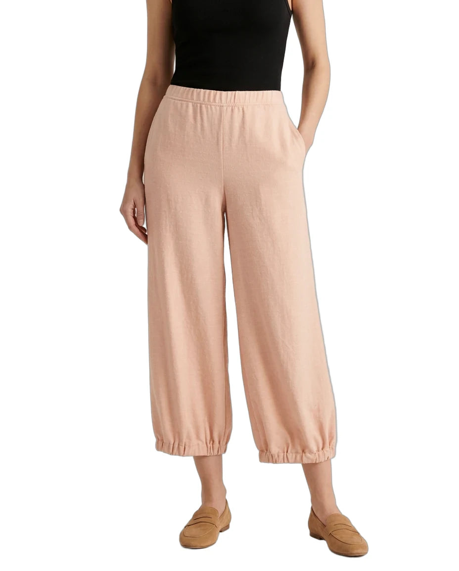 A model wearing light peach wide-leg cropped pants with an elastic waistband and gathered cuffs, paired with a black top and tan loafers, shown against a plain white background.