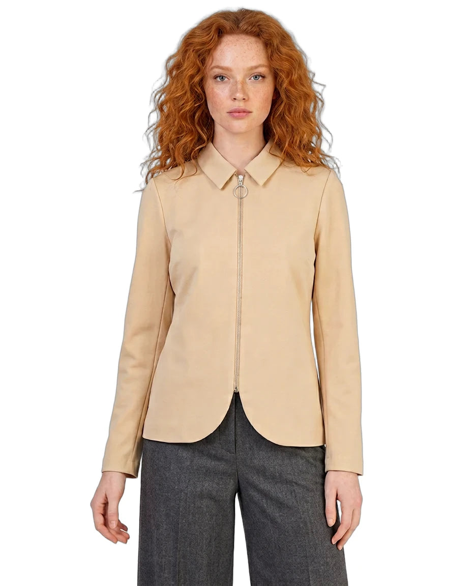 A model with curly red hair wearing a beige zip-up collared jacket and dark gray trousers, photographed against a solid white background.