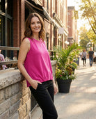 Woman in a pink top standing on a city street with buildings and plants in the background