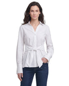 Woman wearing a Calvin Klein white tie-waist blouse and blue jeans on a white background