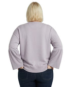 Person wearing a light purple Calvin Klein sweater with ruffled sleeves on a white background