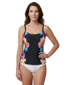 Woman wearing a Calvin Klein black tankini top with colorful floral design and white bottoms on a white background