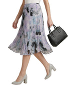 Woman wearing a Calvin Klien floral pleated skirt holding a black handbag on a white background