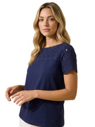 Three-quarter angle portrait of a woman wearing the Charter Club navy blue cotton short-sleeve top with floral eyelet embroidery across the chest and sleeves.
