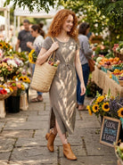 Woman walking through a farmers market with a basket, surrounded by flowers and produce.